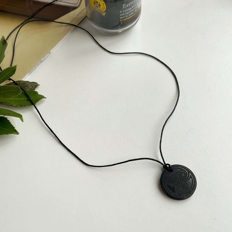 Puede incluir: Un collar negro con un colgante redondo con un dise&ntilde;o de nudo celta tallado.