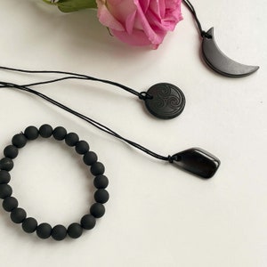 Puede incluir: Un conjunto de tres piezas de joyer&iacute;a de obsidiana negra: un brazalete, un collar con un colgante circular y un collar con un colgante de media luna.