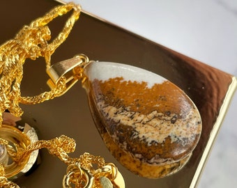May include: A gold chain necklace with a teardrop-shaped pendant made of brown, white, and black patterned stone.