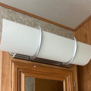 May include: A rectangular light fixture with a white fabric shade and silver metal accents. The fixture is mounted above a wooden cabinet. The shade is approximately 24 inches long.