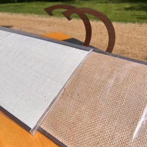 K&ouml;nnte beinhalten: Ein rechteckiges Pr&auml;sentationsboard mit zwei unterschiedlich texturierten Fl&auml;chen in Hellgrau und Beige, eingefasst in einen dunklen Rahmen. Zwei geschwungene, dunkelbraune Holzgriffe sind an der Oberkante des Boards befestigt.