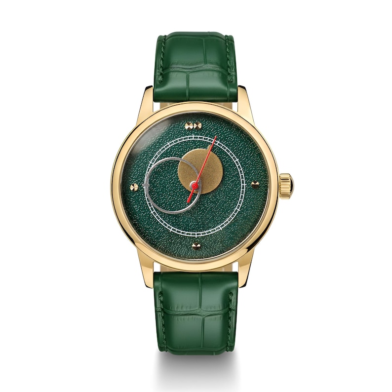 May include: A gold-toned wristwatch with a green face and a green leather band. The watch face features a gold circle, a red hand, and a white circular design. The watch has a gold-toned case and a green leather band.