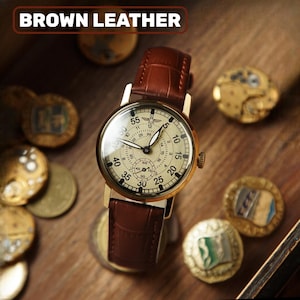 May include: A gold-coloured wristwatch with a cream face and brown leather strap. The watch face has multiple dials and numbers. The text "BROWN LEATHER" is at the top of the image. Antique coins surround the watch.