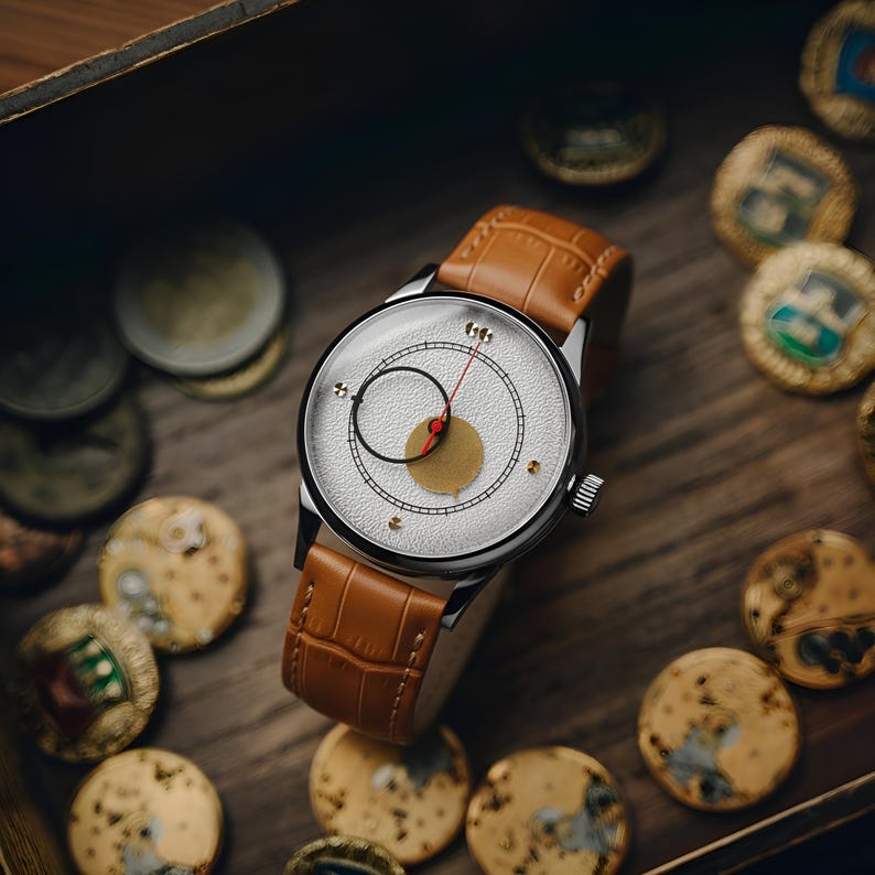 May include: A silver wristwatch with a textured white face, black and red accents, and a brown leather band. The watch is surrounded by gold-colored coins, set in a wooden box.