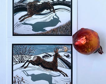 Pack of 8 Christmas cards, 2 designs,  featuring a leaping hare and deer crossing a snowy landscape