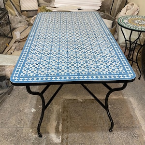 May include: Rectangular outdoor table with a blue and white tile mosaic top and black metal legs. The table's surface features a repeating geometric pattern. The table is approximately 152 cm long and 76 cm wide.