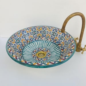 Puede incluir: Un lavabo decorativo de cerámica con un patrón detallado y colorido en verde azulado, amarillo y rojo. El lavabo tiene un grifo de latón. El diseño del lavabo presenta un motivo floral central y patrones geométricos.