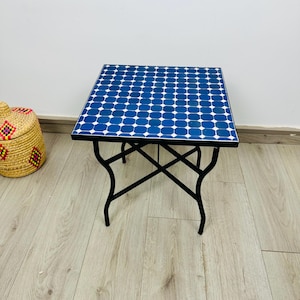 May include: A small square table with a blue and white tiled top and a black metal frame. The table has a geometric pattern of circles.
