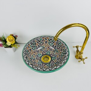 May include: A ceramic sink with a green, blue, and brown geometric pattern. The sink has a brass faucet with a curved spout.
