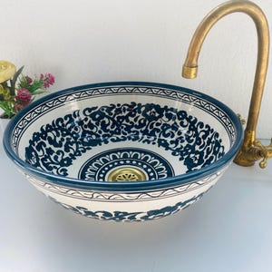 May include: A white ceramic sink with a blue and white floral pattern. The sink has a brass faucet with a curved spout.
