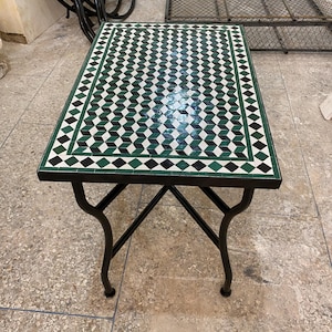 Peut inclure: Table rectangulaire en mosaïque avec un cadre en métal noir. Le plateau présente un motif géométrique de carreaux verts, noirs et blancs. La table mesure environ 76 cm de long et 51 cm de large.