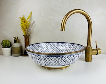 Può includere: Un lavabo in ceramica bianca con un motivo geometrico blu e bianco. Il lavabo ha un bordo dorato e una base dorata. Un rubinetto dorato è montato sopra il lavabo.