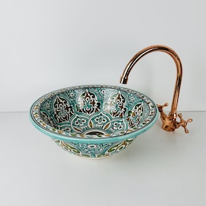 Puede incluir: Un lavabo de cerámica con un patrón floral verde y marrón. El lavabo es redondo y tiene un grifo de cobre.