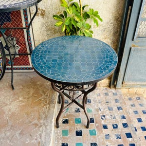 May include: A small, round table with a blue mosaic tile top and a black metal base. The table is sitting on a tiled floor.
