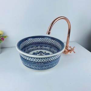 Może przedstawiać: Biała ceramiczna umywalka z niebiesko-białym wzorem. Umywalka ma miedzianą baterię z jedną dźwignią.