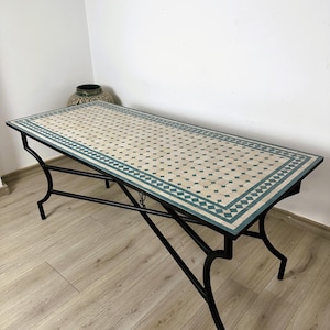 May include: A rectangular table with a mosaic tile top in cream and teal. The table has a black wrought iron base with curved legs. The mosaic tile design features small square and diamond shapes. The table is approximately 152 cm long.