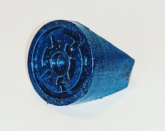 Può includere: Un anello blu con un designo in rilievo dettagliato di un simbolo con un cerchio al centro. L'anello è fatto di un materiale testurizzato.