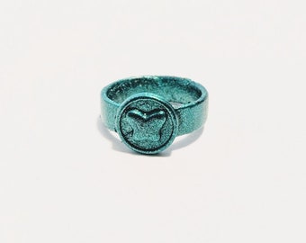 Può includere: Anello turchese con un design circolare che presenta una farfalla stilizzata. L'anello è realizzato in un materiale testurizzato.