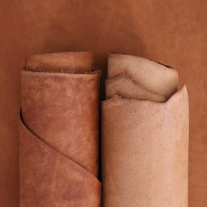 May include: Two rolls of leather, one brown and one light brown, are shown side by side. The leather is folded and has a natural, textured surface.