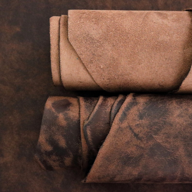 May include: Two rolls of leather material are positioned horizontally. The top roll is a light tan color with a matte, suede-like texture. The bottom roll is a dark chocolate brown color with a distressed, mottled finish and visible grain.
