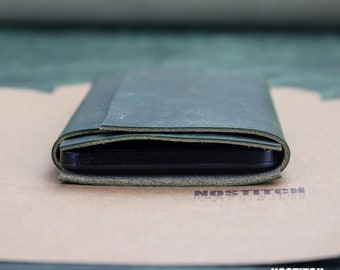 May include: A dark green leather wallet folded closed with the brand name "NOSTITCH handcrafted leathergoods" embossed on the bottom flap.