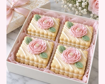 May include: A white gift box containing four square sandwich cookies. Each cookie features a scalloped edge, white icing drizzle, and a central pink frosting rose with two green leaves. The cookies are nestled in pink tissue paper.