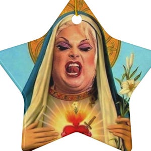 May include: A star-shaped Christmas ornament featuring a woman with a crown of thorns and a red heart with a sword through it. The woman is wearing a blue robe and has a white halo. The background is a blue sky with white clouds.