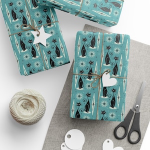 Pode incluir: Papel de embrulho azul com um padrão repetido de gatos pretos e estrelas brancas. O papel está embrulhado em torno de uma caixa de presente com uma etiqueta em forma de estrela branca e um laço de corda marrom.