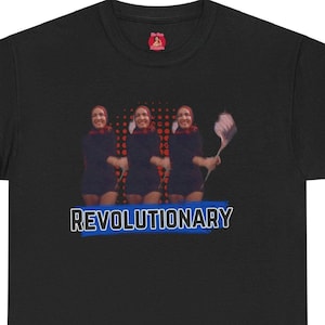 May include: Black t-shirt featuring a graphic of three women in red dresses and blue scarves. The women are holding a white feather duster. The text "REVOLUTIONARY" is printed in blue on a white background.
