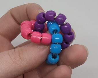 May include: A colorful beaded fidget toy with purple, pink, and blue beads strung on a wire. The beads are arranged in a spiral pattern.