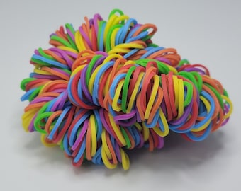 May include: A large pile of colorful rubber bands in a rainbow of colors, including red, orange, yellow, green, blue, and purple.