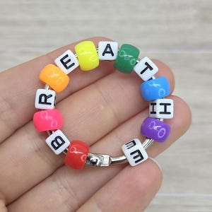 May include: A rainbow-coloured beaded keyring spelling "Breathe". The beads are in various colours, with white lettered cubes. The keyring is attached to a silver metal ring.