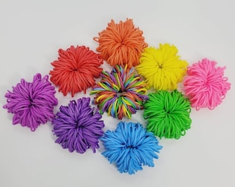 May include: A collection of colorful rubber band flowers in various shades, including red, orange, yellow, pink, purple, blue, and green. The flowers are arranged on a white surface, creating a vibrant and playful display. Each flower is approximately 3 inches in diameter.