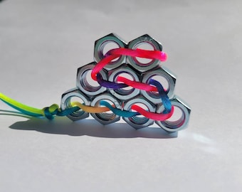 May include: A pyramid of silver hex nuts is interwoven with colorful cords in shades of pink, purple, blue, yellow, and green. The cords are knotted at the end, creating a unique and eye-catching design.
