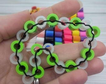 May include: A green and white beaded bracelet with a black elastic string. The beads are round and have a hole in the center. The bracelet is made of plastic.