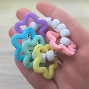 May include: A circular bracelet featuring a series of colorful star-shaped charms in purple, blue, teal, yellow, and pink, interspersed with small, round, opaque white beads strung on a flexible cord to form a vibrant, multi-colored accessory.