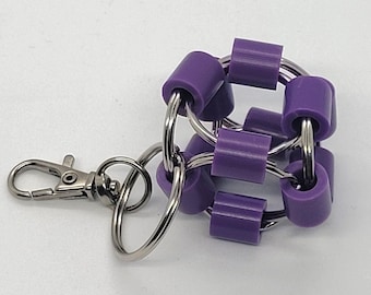 May include: A purple and silver keychain featuring a spherical design made of purple cylindrical beads connected by silver rings. A silver clasp is attached for easy attachment to bags or keys. The keychain is a unique accessory.