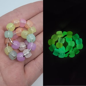 Pode incluir: Um brinquedo de fidget colorido feito de contas de cores pastel. As contas são dispostas em um círculo e conectadas por um anel de metal. O brinquedo brilha no escuro, como mostrado na segunda imagem.