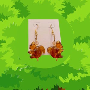 May include: A pair of dangle earrings featuring amber-colored glass squirrel charms with gold-tone hooks and crystal accents.