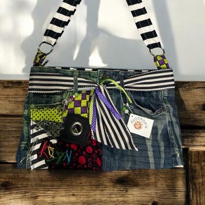 May include: A denim handbag with a black and white striped strap and accents. The bag features patches of various patterns, including polka dots, checkerboard, and embroidery. A tag reads "Augsborn".