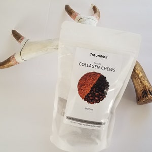 May include: A clear pouch of "Multi Collagen Chews" in mocha flavor, with a graphic of coffee beans and a brown powder. The pouch is positioned in front of a decorative antler. The text "TotumVos" is at the top of the pouch.