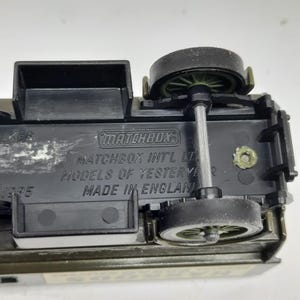 Puede incluir: La parte inferior de un veh&iacute;culo de juguete de metal fundido con componentes y ruedas de pl&aacute;stico negro. El texto en relieve dice Matchbox, Matchbox Int'l Ltd, Models of Yesteryear y Made in England, con el a&ntilde;o 1985 visible a la izquierda.