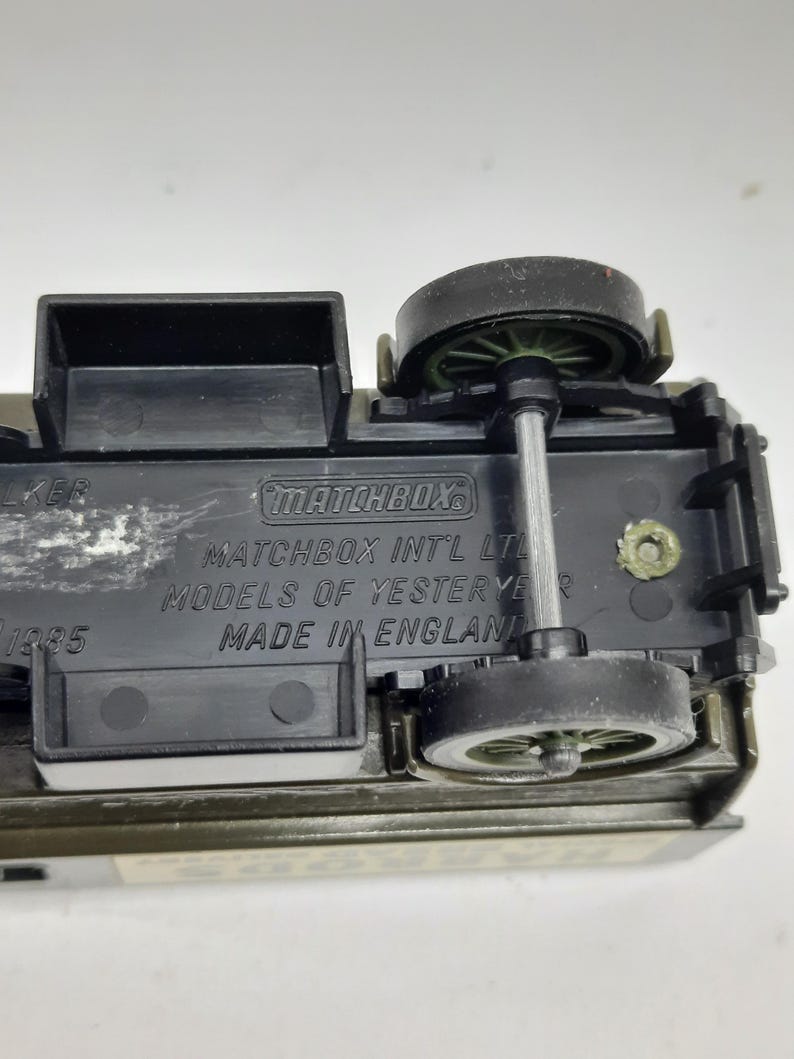Puede incluir: La parte inferior de un veh&iacute;culo de juguete de metal fundido con componentes y ruedas de pl&aacute;stico negro. El texto en relieve dice Matchbox, Matchbox Int'l Ltd, Models of Yesteryear y Made in England, con el a&ntilde;o 1985 visible a la izquierda.