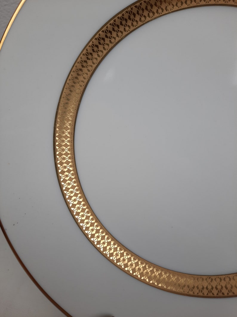 Puede incluir: Un plato de cer&aacute;mica blanco con un borde dorado y un patr&oacute;n geom&eacute;trico. El plato es perfecto para servir una variedad de platos.