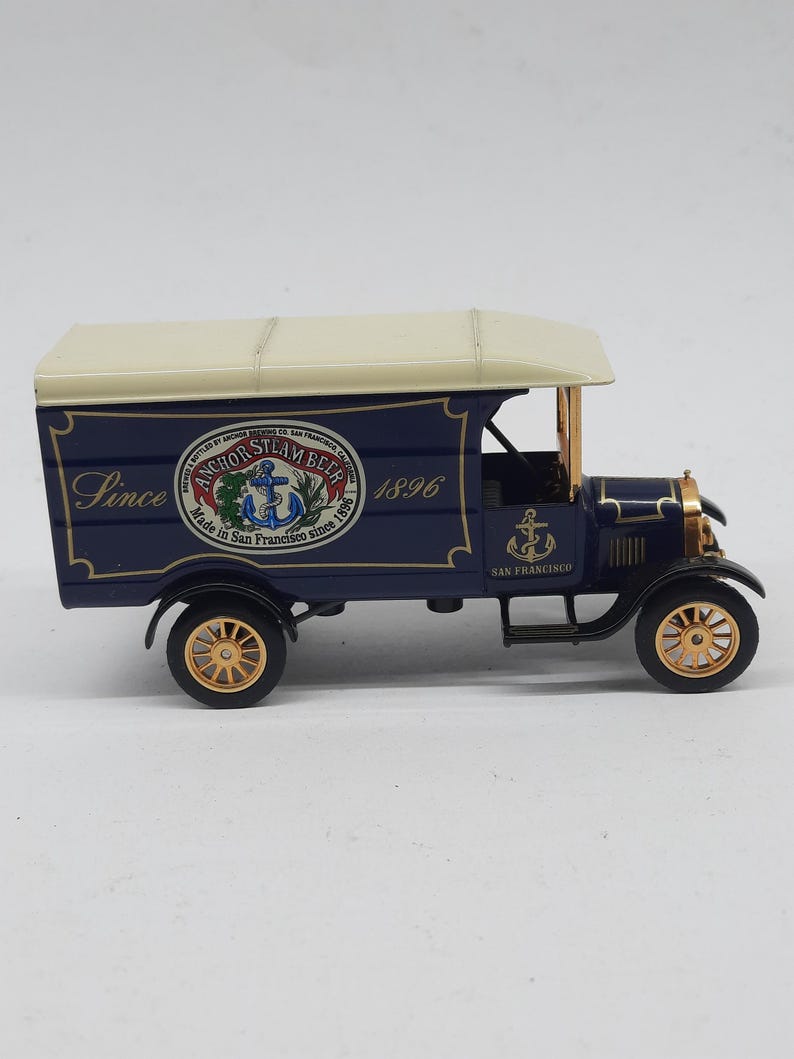 May include: A dark blue vintage-style delivery truck model with a cream-colored roof. The side features the text "Since 1896" and a circular logo reading "Anchor Steam Beer Made in San Francisco since 1896" with an anchor graphic and gold wheels.