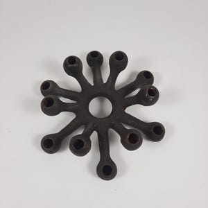 Può includere: Un portacandele a forma di stella marrone scuro con 12 aperture circolari per candele. Il portacandele ha un'apertura centrale circolare ed è realizzato in un materiale solido. Il design è simmetrico e organico.