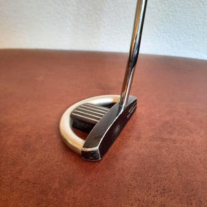 Könnte beinhalten: Ein schwarzer und silberner Golf-Putter mit schwarzem Griff und dem Schriftzug "Scotty Cameron" an der Seite.