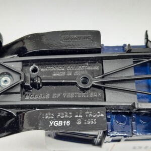 May include: The underside of a blue and black die-cast toy truck featuring the embossed text Matchbox Collectibles, Made in China, Models of Yesteryear, 1932 Ford AA Truck, and YGB16. The chassis is black metal with visible screw holes.