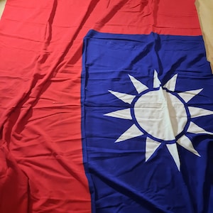 May include: A large, folded flag of the Republic of China, also known as the Taiwanese flag. The flag is red with a blue canton featuring a white sun with 12 points.