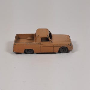 Puede incluir: Un camión de juguete antiguo de color naranja apagado. El camión tiene un diseño clásico con cabina y caja de carga. Las ruedas son negras y la pintura muestra signos de desgaste, lo que sugiere que es un modelo más antiguo.